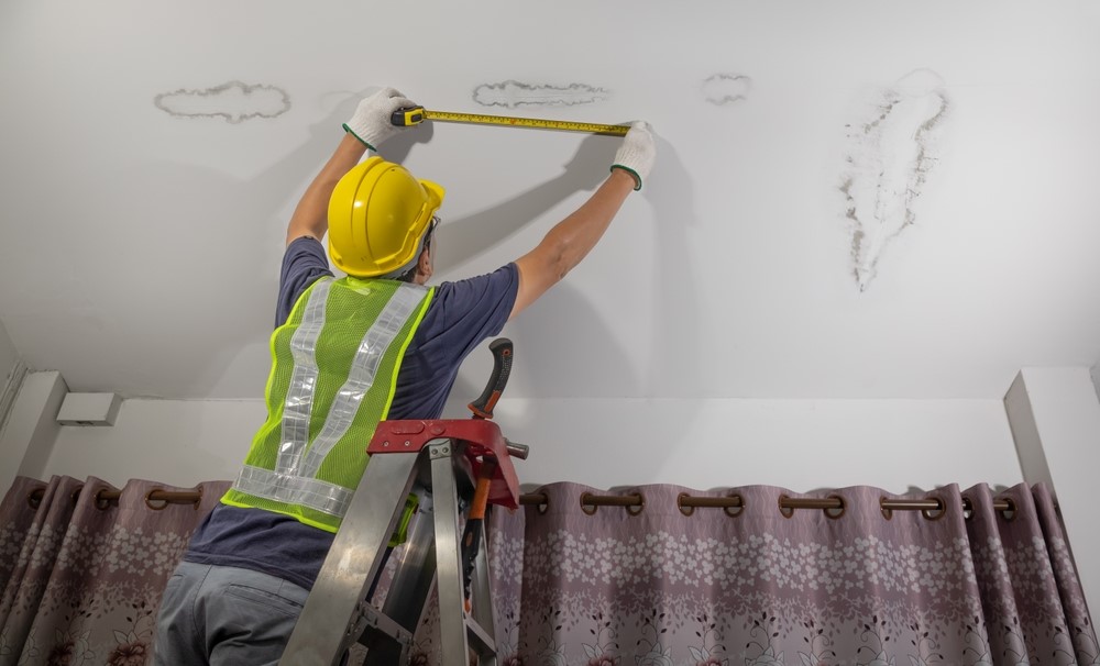 Worker measuring water damage on a ceiling caused by water leaks