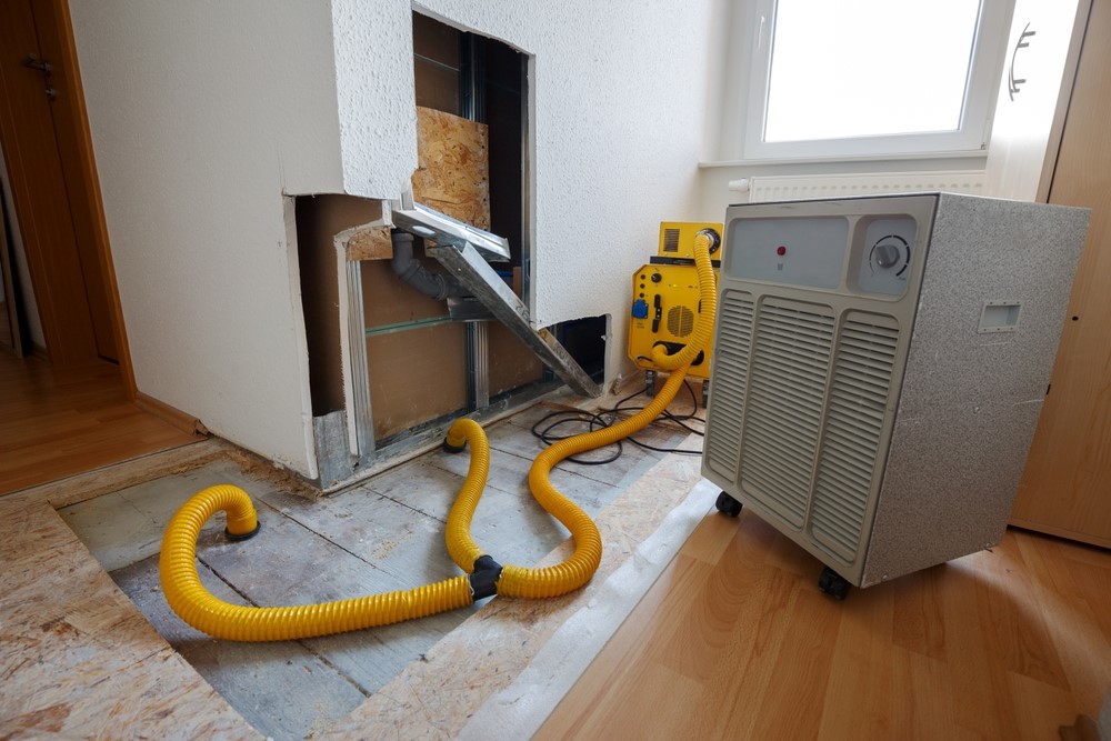 Water damage restoration equipment being used in a home to dry out a wall and floor after water damage